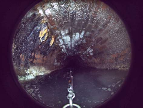Photo in an underground, brick sewer of an assessment of conditions inside the pipe. Raw sewage flows as a robotic camera scans the area for corrosion, leaks, debris, etc. This work was completed in November 2024 as part of a condition assessment of the Peabody-Salem Interceptor pipes.